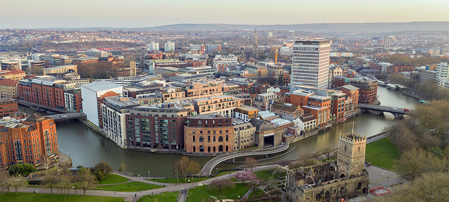 Aerial view of Bristol city centre featuring the River Avon, modern waterfront buildings, historic architecture, and green open spaces, representing the vibrant student and cultural life of Bristol, UK.